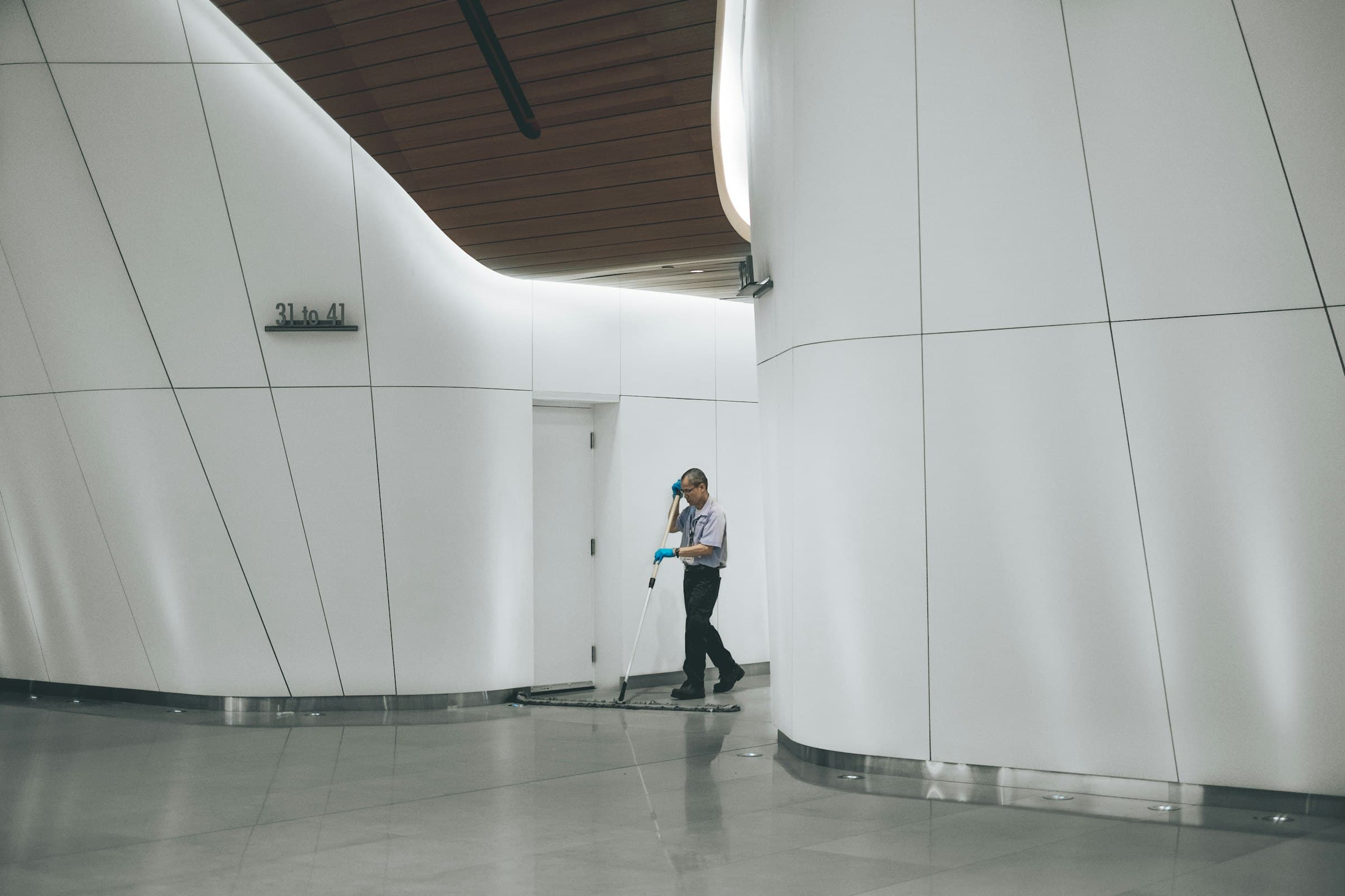 Mitarbeiter reinigt mit einem Wischmopp einen hellen Flur in einem modernen Gebäude